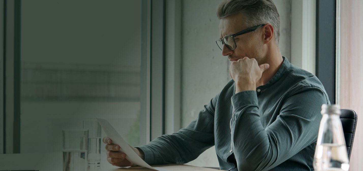 Man in glasses sitting at table, holding and reading a paper