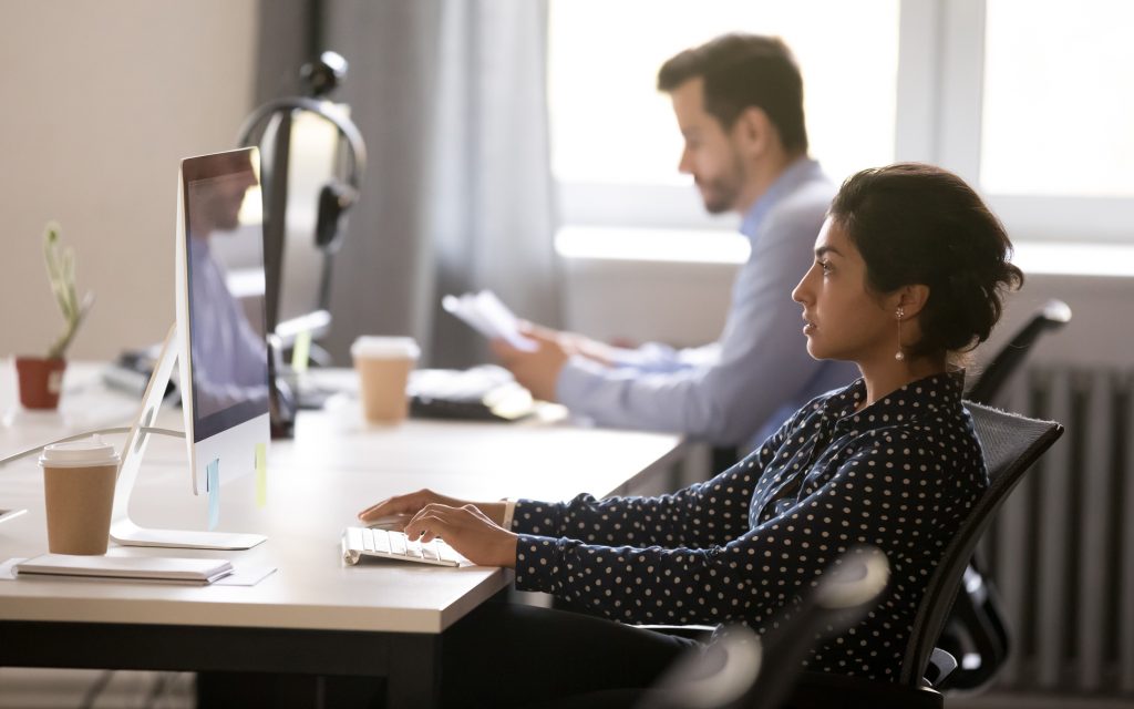 Two people working in an office, the person in the foreground is on their computer.