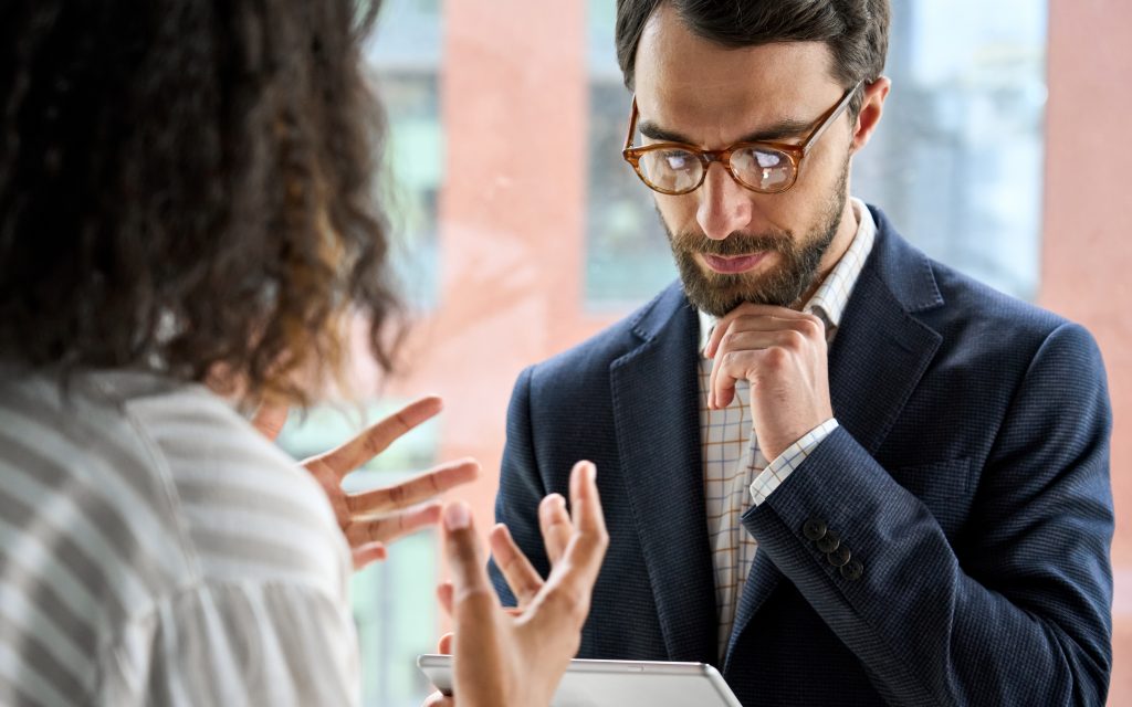 Two people having an animated conversation. One is moving their hands and the other is looking down at a tablet.