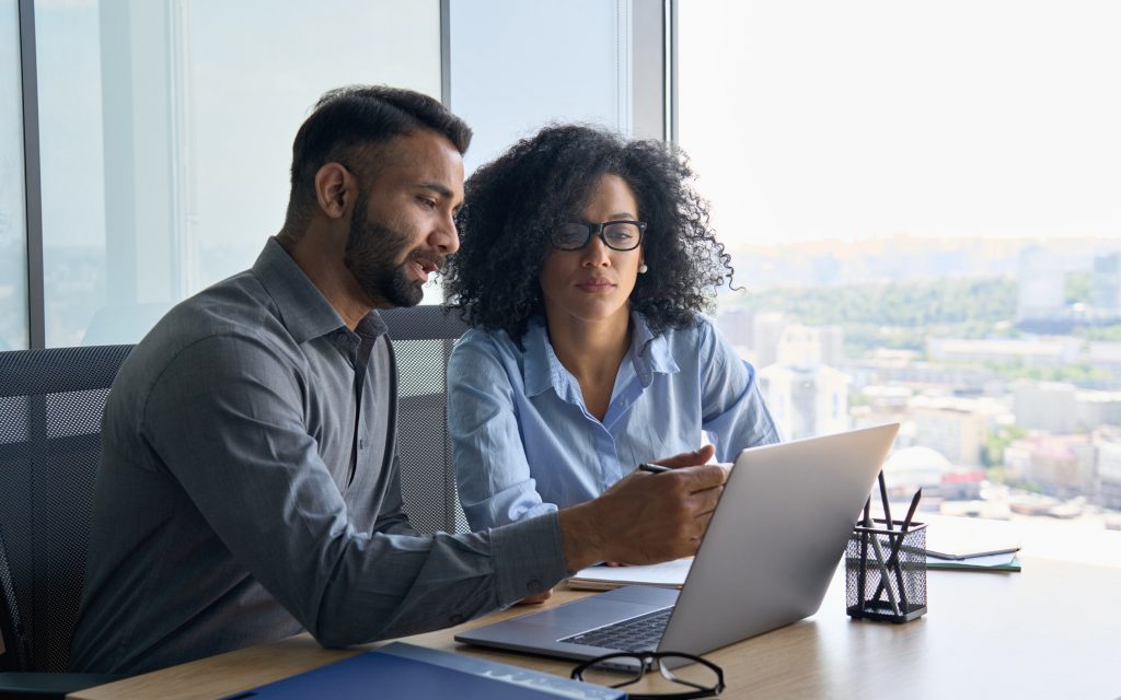 Two people in an office looking at a laptop together.