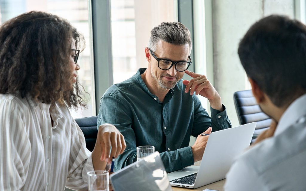 A group of three people having a conversation and looking at a laptop.